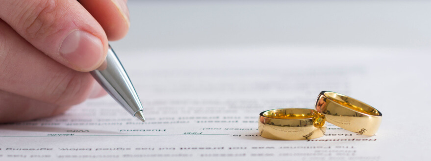 person signing divorce agreement with wedding rings in foreground