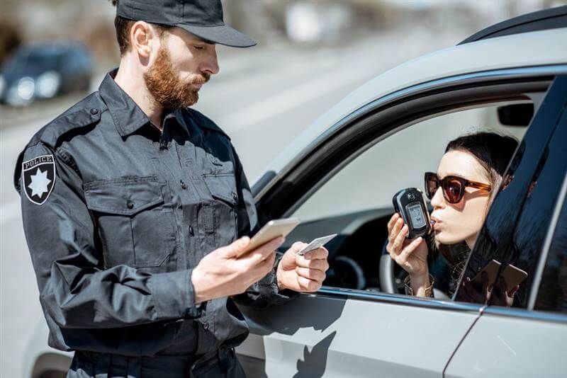 Policeman checking woman driver for alcohol intoxication with special device while stopped for violation traffic rules on the roadside
